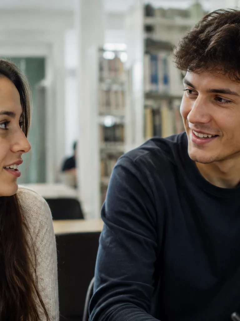 Duas participantes conversando de pé no corredor entre prateleiras de livros